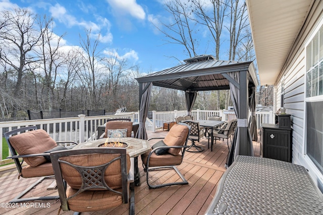 deck with an outdoor fire pit, fence, a gazebo, outdoor dining space, and a trampoline