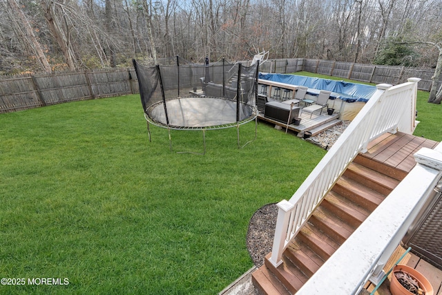 view of yard featuring a deck, a trampoline, a fenced backyard, and a fenced in pool