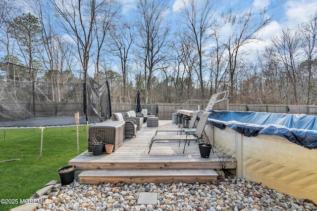 wooden terrace featuring a trampoline, a fenced in pool, a fenced backyard, and a lawn