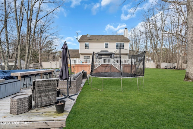 back of house with a trampoline, a fenced backyard, a lawn, and a chimney