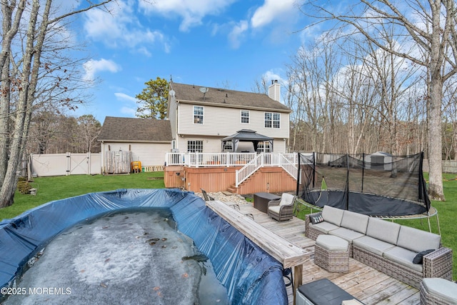 back of property with a trampoline, a gazebo, an outdoor hangout area, a gate, and a wooden deck