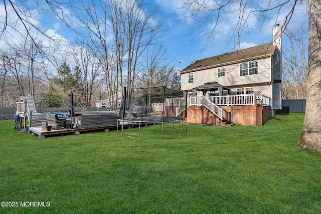 rear view of house featuring a yard, a wooden deck, a trampoline, and a gazebo