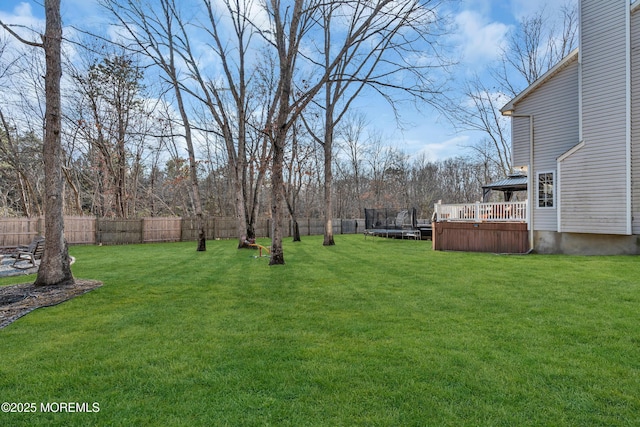 view of yard featuring a deck, a trampoline, and a fenced backyard