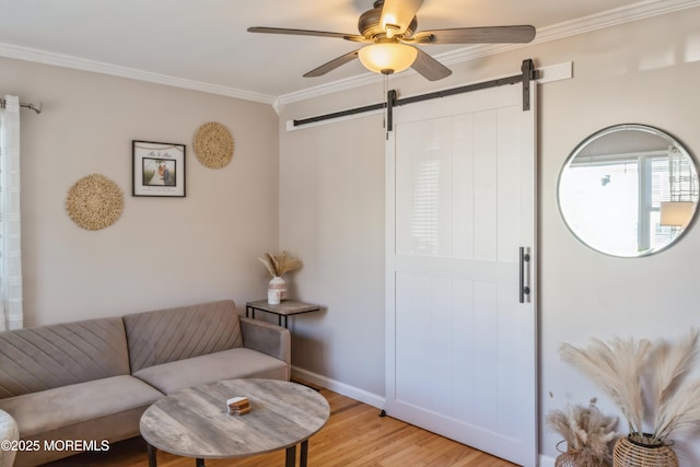 living area featuring ceiling fan, a barn door, light wood-style flooring, baseboards, and crown molding