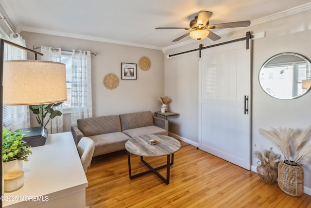 living room featuring a barn door, baseboards, ceiling fan, light wood-style flooring, and crown molding