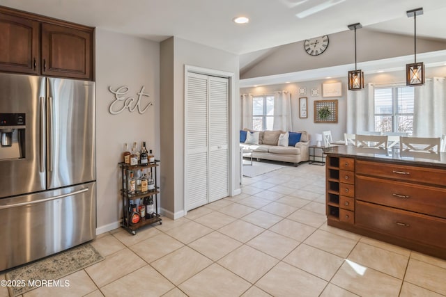 kitchen with light tile patterned floors, lofted ceiling, hanging light fixtures, stainless steel fridge with ice dispenser, and dark countertops