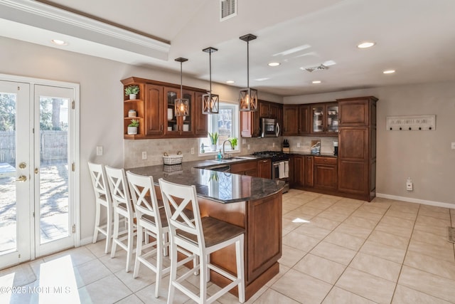 kitchen with a peninsula, a sink, visible vents, appliances with stainless steel finishes, and glass insert cabinets