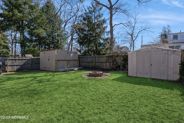 view of yard featuring a fire pit, a fenced backyard, a storage unit, and an outdoor structure