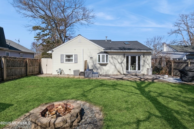 back of property with an outdoor fire pit, a fenced backyard, a lawn, and central air condition unit