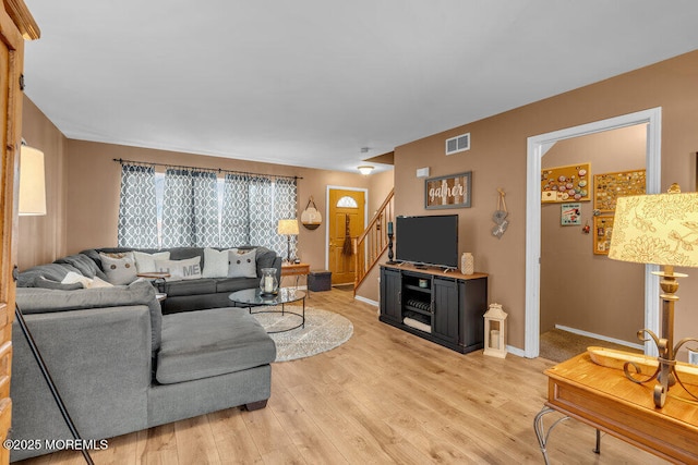 living room with baseboards, visible vents, stairway, and light wood finished floors