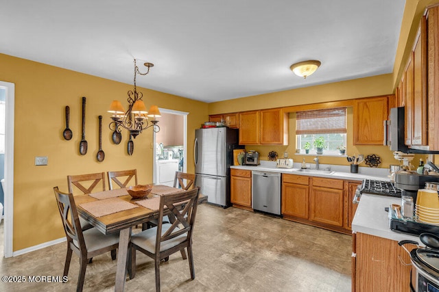 kitchen featuring pendant lighting, washer / clothes dryer, light countertops, appliances with stainless steel finishes, and a sink