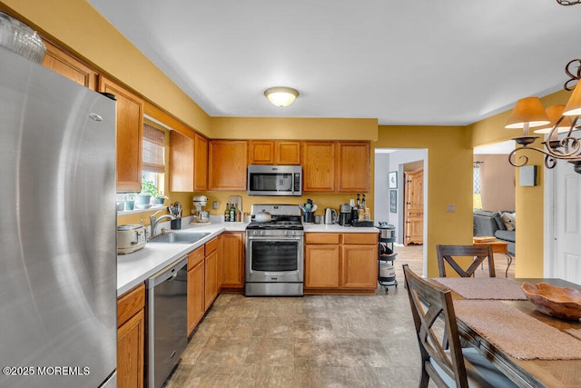 kitchen featuring brown cabinetry, decorative light fixtures, stainless steel appliances, light countertops, and a sink