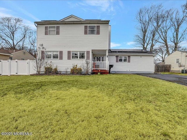 back of property featuring solar panels, a lawn, cooling unit, and fence