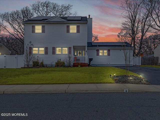 traditional-style home with aphalt driveway, solar panels, a lawn, a gate, and fence