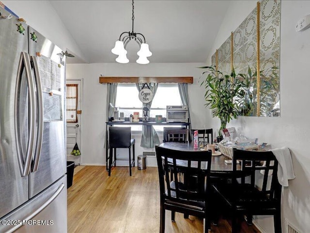 dining space with lofted ceiling, light wood-style floors, and a notable chandelier