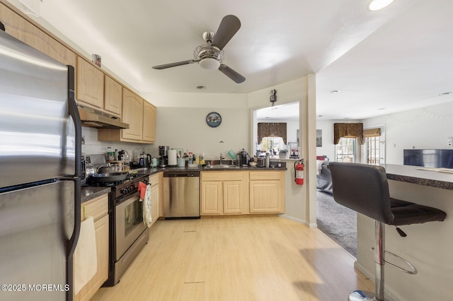 kitchen featuring dark countertops, under cabinet range hood, appliances with stainless steel finishes, and light brown cabinetry