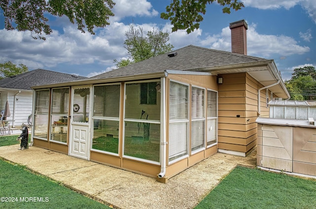 back of property with a sunroom, a shingled roof, and a chimney