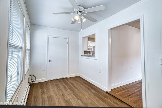 unfurnished bedroom featuring baseboard heating, wood finished floors, a ceiling fan, and baseboards