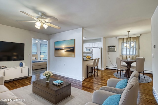 living room with an AC wall unit, dark wood finished floors, baseboards, and ceiling fan with notable chandelier