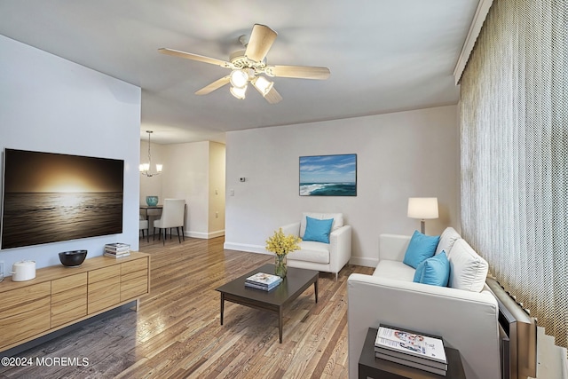 living room with ceiling fan with notable chandelier, wood finished floors, and baseboards