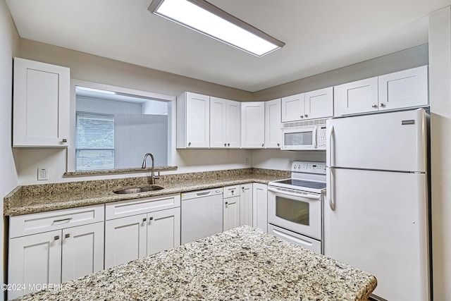 kitchen with white appliances, white cabinetry, light stone counters, and a sink