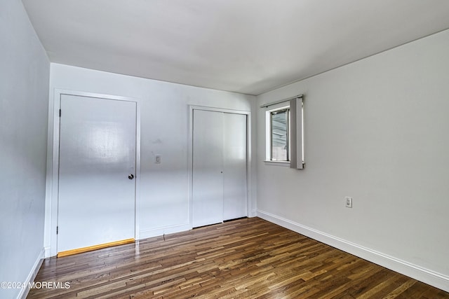 unfurnished bedroom with a closet, baseboards, and dark wood-style flooring