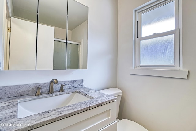 bathroom with a shower with shower door, vanity, and toilet