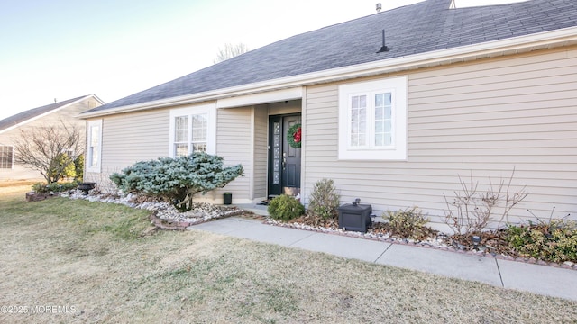 entrance to property featuring a yard and roof with shingles