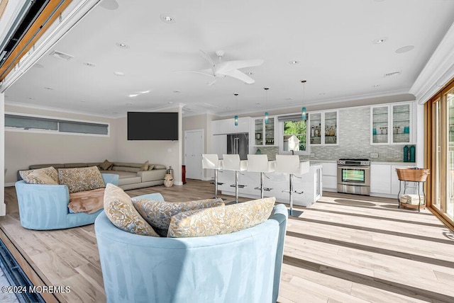 living area with a ceiling fan, light wood-type flooring, visible vents, and crown molding