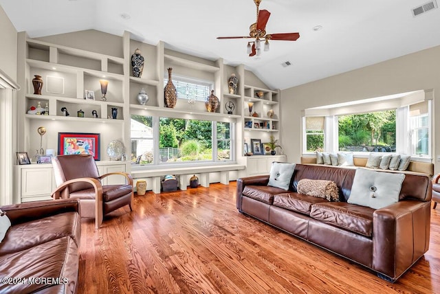 living room with built in shelves, a wealth of natural light, visible vents, and vaulted ceiling