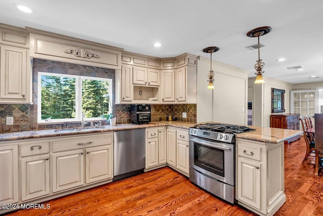 kitchen featuring a peninsula, appliances with stainless steel finishes, a sink, and light wood-style flooring