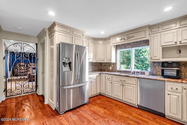 kitchen featuring tasteful backsplash, appliances with stainless steel finishes, a sink, and light wood-style floors