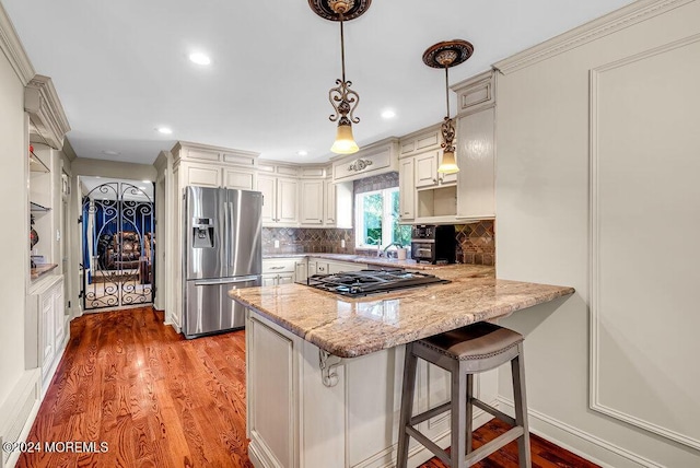 kitchen featuring light stone counters, stainless steel refrigerator with ice dispenser, gas stovetop, light wood finished floors, and a peninsula