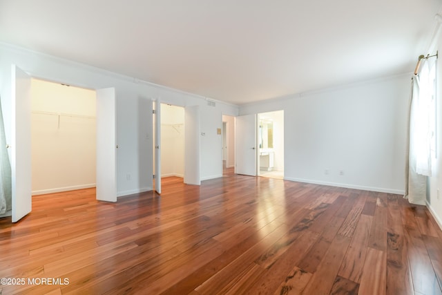 unfurnished bedroom with light wood finished floors, visible vents, baseboards, ornamental molding, and a spacious closet