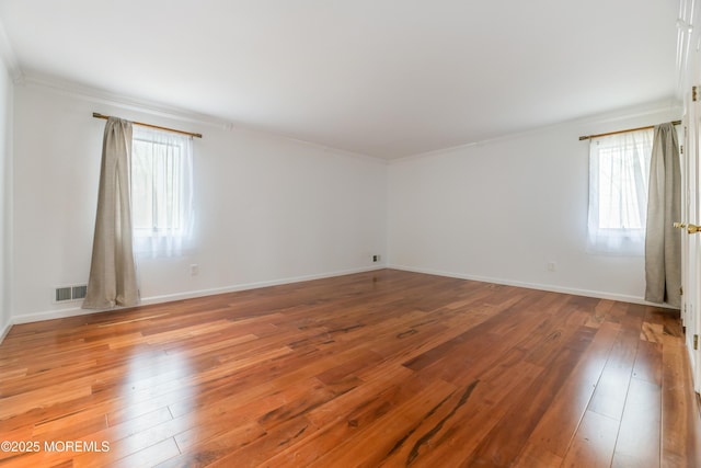 empty room featuring wood-type flooring, visible vents, baseboards, and ornamental molding