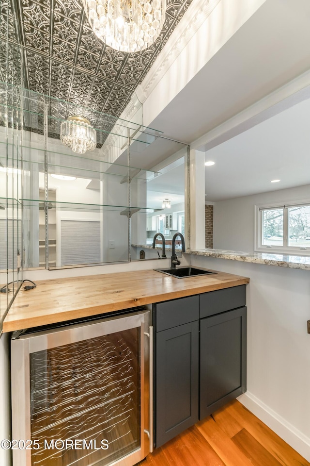 bar featuring wine cooler, a sink, baseboards, light wood finished floors, and an ornate ceiling