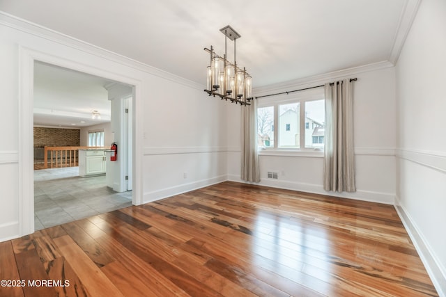 empty room featuring baseboards, visible vents, ornamental molding, wood finished floors, and an inviting chandelier