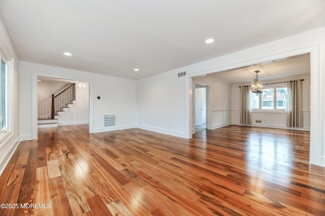 unfurnished living room with light wood finished floors, visible vents, stairway, a chandelier, and baseboards