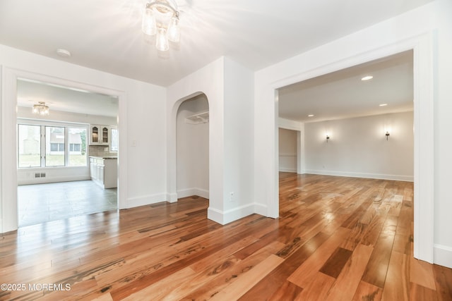 empty room with arched walkways, recessed lighting, light wood-style flooring, and baseboards