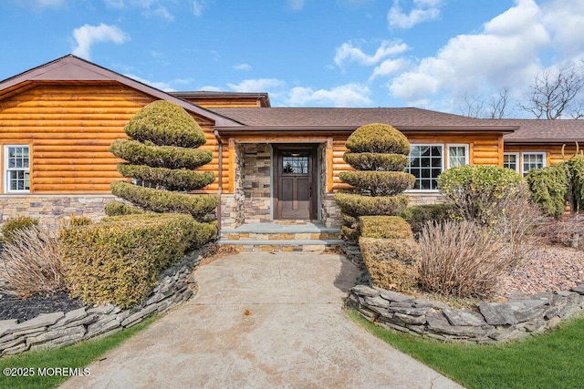 cabin featuring stone siding and a shingled roof