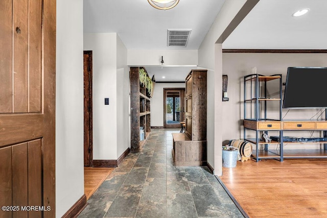 hall with ornamental molding, wood finished floors, visible vents, and baseboards