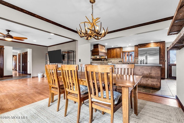 dining space featuring ceiling fan with notable chandelier, light wood-type flooring, baseboards, and crown molding