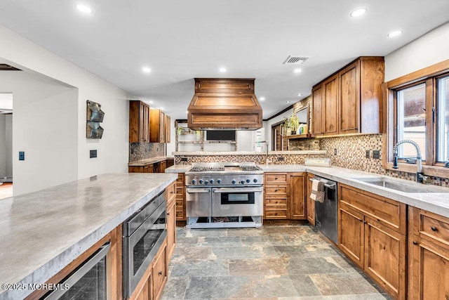 kitchen featuring visible vents, brown cabinetry, appliances with stainless steel finishes, custom exhaust hood, and a sink