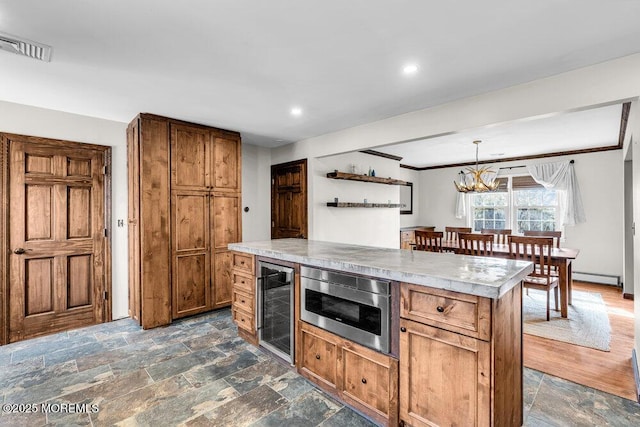 kitchen with stone tile floors, a baseboard radiator, stainless steel microwave, visible vents, and beverage cooler