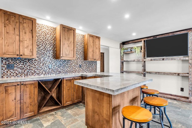 kitchen with a breakfast bar, stone finish floor, brown cabinetry, and decorative backsplash