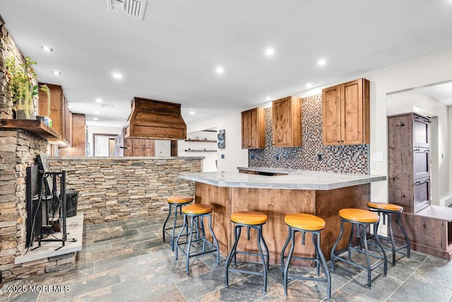 kitchen with brown cabinets, light countertops, visible vents, decorative backsplash, and a peninsula