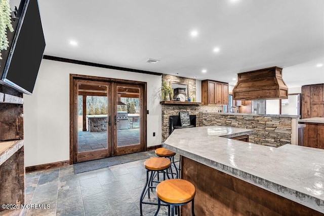 kitchen with stone tile floors, custom range hood, baseboards, and decorative backsplash