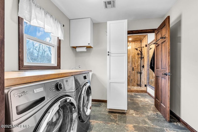 laundry room featuring washing machine and dryer, visible vents, baseboards, cabinet space, and stone finish floor