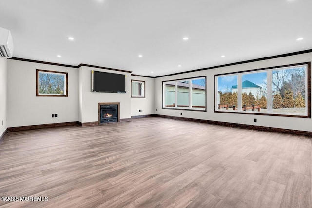 unfurnished living room featuring a glass covered fireplace, plenty of natural light, wood finished floors, and baseboards