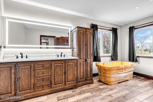 full bath with a freestanding tub, baseboards, a sink, and wood finished floors